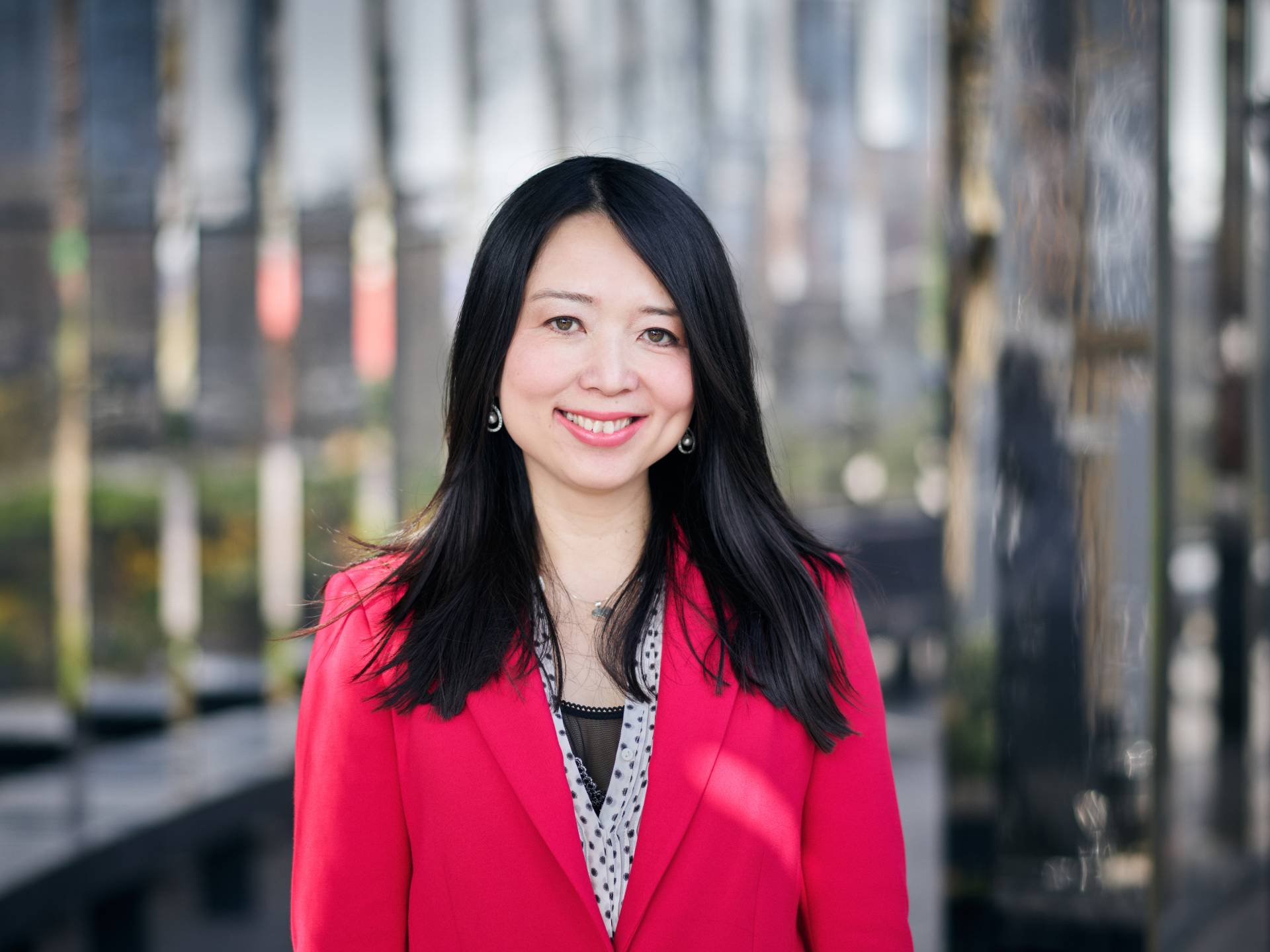 A smiling headshot of Dr. Chen Mao Davies, Founder and CEO of Anya. She has long dark hair, and is wearing a vibrant magenta blazer over a polka-dotted blouse. She is looking directly at the camera in front of an urban background.